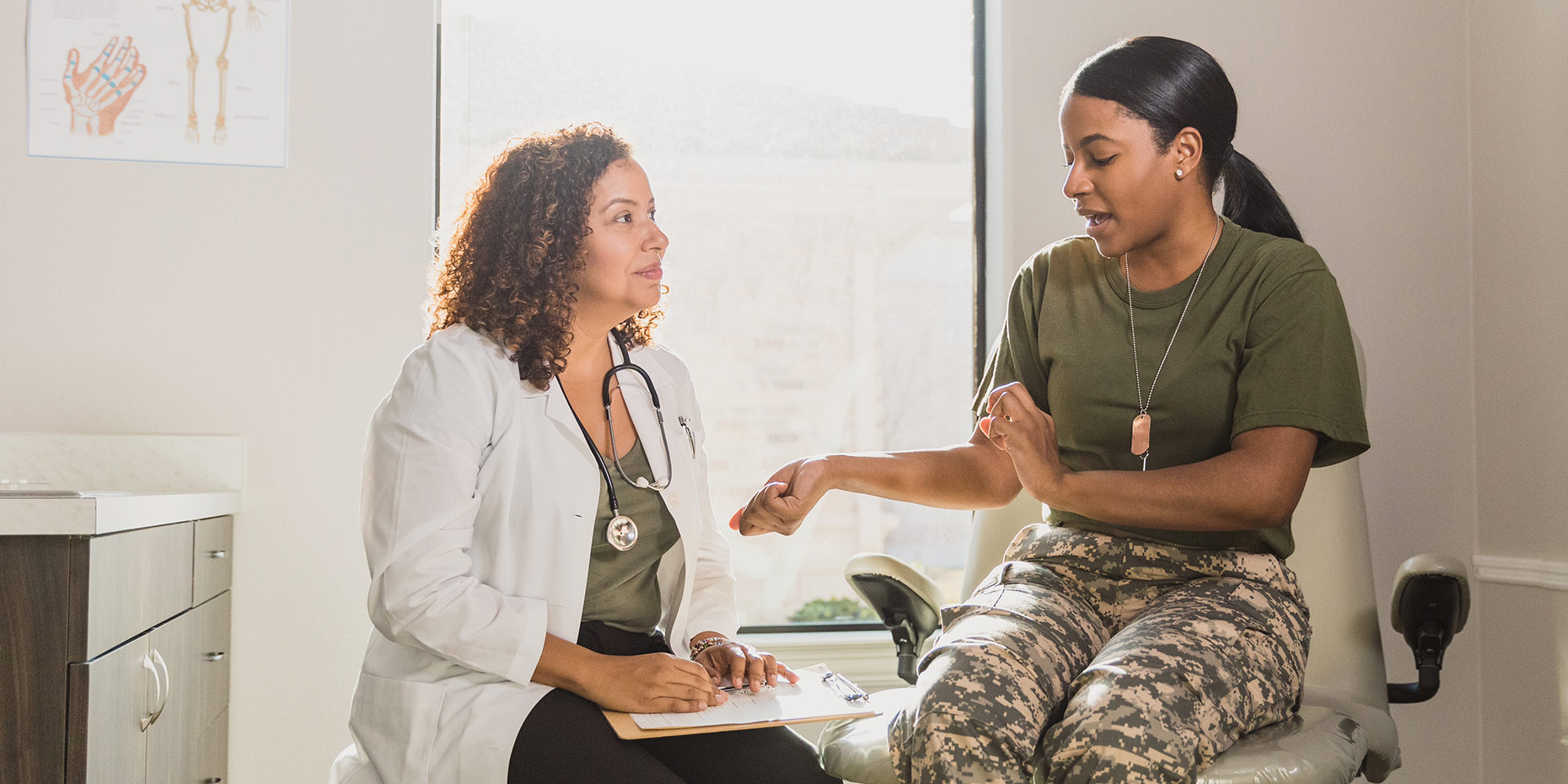 Doctor looking at woman in military uniform while she talks and points to her arm