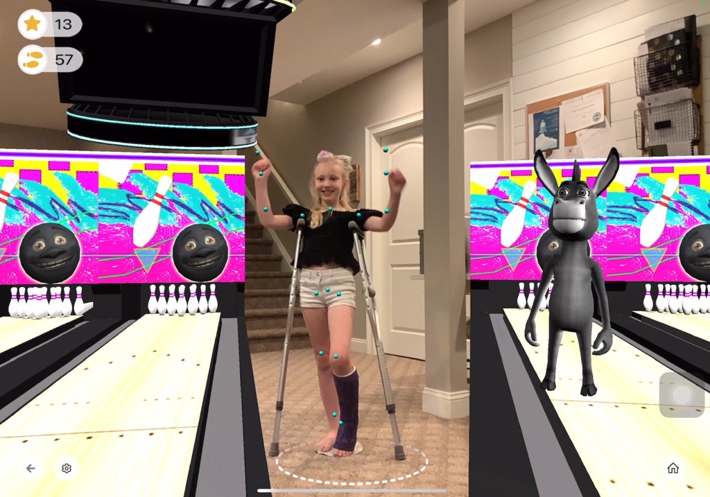 Young girl with crutches playing a virtual game of bowling, smiling.