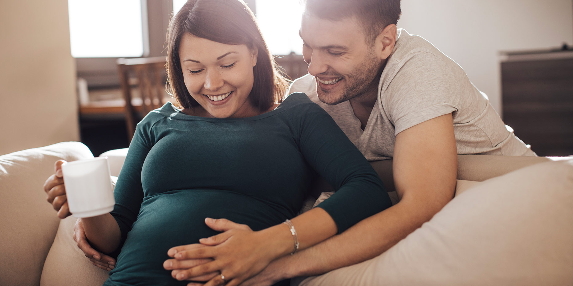 Pregnant woman smiling hands on belly looking down man beside her smiling