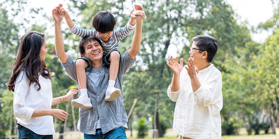 A family is walking together outside. A child is the shoulders of their father.