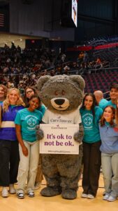 Cuddles poses with students With sign that says It's ok to not be ok.