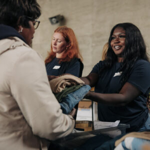 Smiling female volunteer giving donated clothes to homeless woman at community center